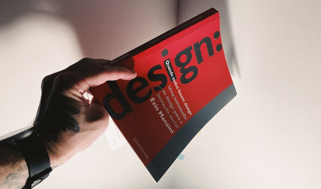 Tattooed hand holding a red book about design.